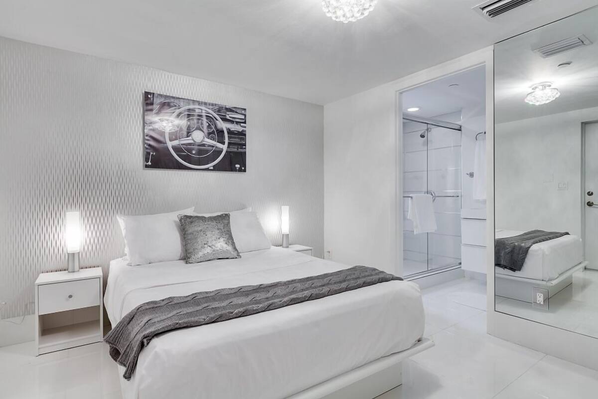 Un dormitorio moderno con una cama grande, mesitas de noche, un espejo y una obra de arte en la pared.