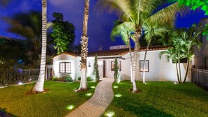 A well-lit pathway leading to a white building with a tiled roof, surrounded by palm trees and a neatly trimmed lawn. - Bars B&B South Beach Miami Boutique Hotel (Miami Beach)