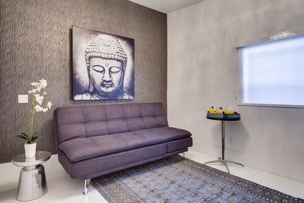 Una sala moderna con un sofá gris, un tapete estampado, un cuadro de Buda, una mesita con una planta en maceta y una lámpara de pie.