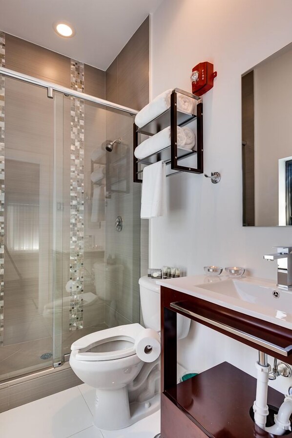 Un baño moderno con cabina de ducha de vidrio, inodoro blanco, tocador de madera con lavamanos y un espejo.