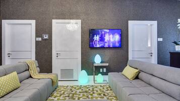 Uma sala de estar moderna com dois sofás cinzas, um tapete estampado, uma televisão de tela plana e uma luminária decorativa na parede.