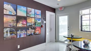 Un hall de hotel con una pared de fotografías del paisaje urbano, una mesa de vidrio con un florero y una puerta que indica "EXIT".