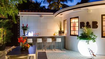 A modern outdoor kitchen area with a dining table, chairs, and a large illuminated planter.