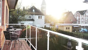 A balcony with a table and chairs, overlooking a residential area with houses and a church steeple. - Hotel Altenwerder Hof (Hamburg)
