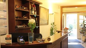 A hotel reception desk with a calendar, a Hotspot sign, a vase with flowers, and a plant. - Hotel Altenwerder Hof (Hamburg)