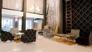 A spacious lobby with multiple seating areas, a chandelier, and a large wall with a geometric pattern. - West Wood Hotel (Nairobi)