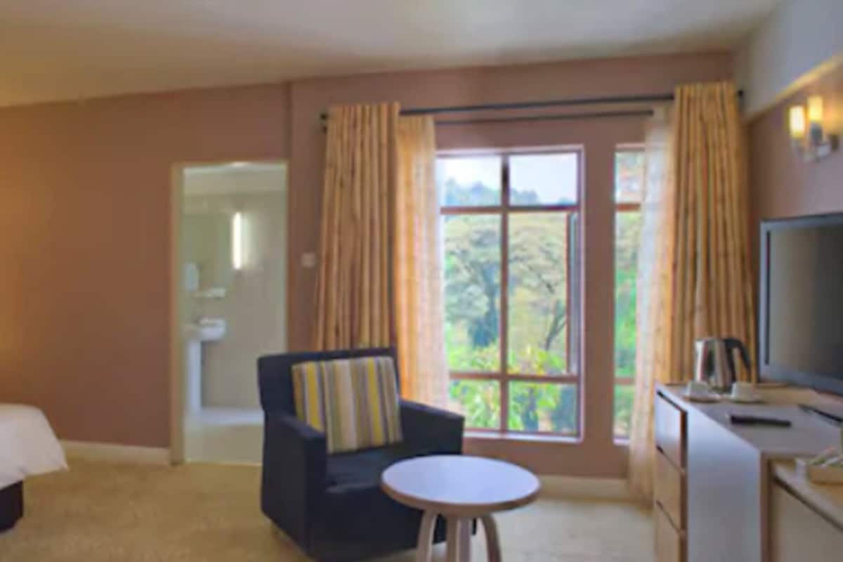A hotel room with a bed, a sofa, a small table, a TV, and a window with curtains.