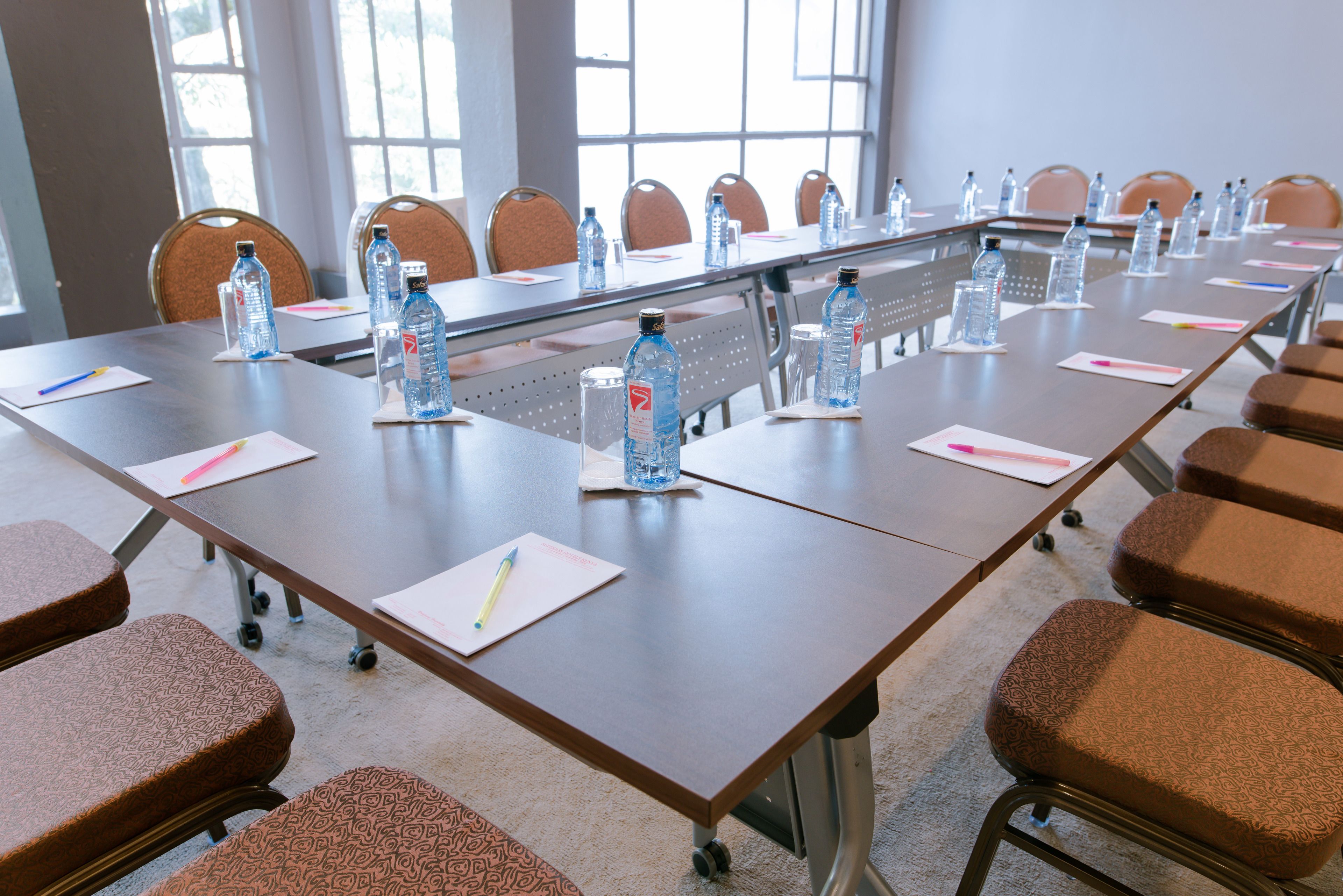 Un salón de conferencias con una larga mesa, sillas, botellas de agua y blocs de notas.