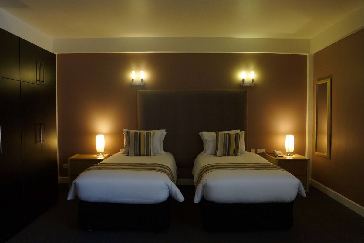 A hotel room with two beds, a dark headboard, bedside lamps, and a framed picture on the wall.