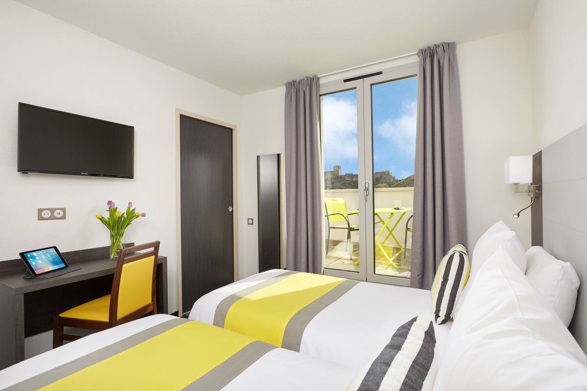 A hotel room with two beds, a desk with a laptop, a TV, and a view of the outdoors.