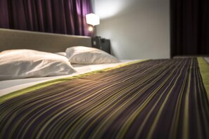 A hotel room with a bed, pillows, and a striped bedspread. - Hôtel Astrid (Lourdes)