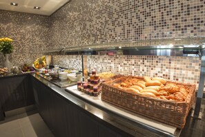 A buffet area with a variety of food items and a decorative mosaic backsplash. - Hôtel Astrid (Lourdes)