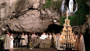 A group of people in religious attire gathered around a lit candle display in a cave-like setting. - Hôtel Astrid (Lourdes)