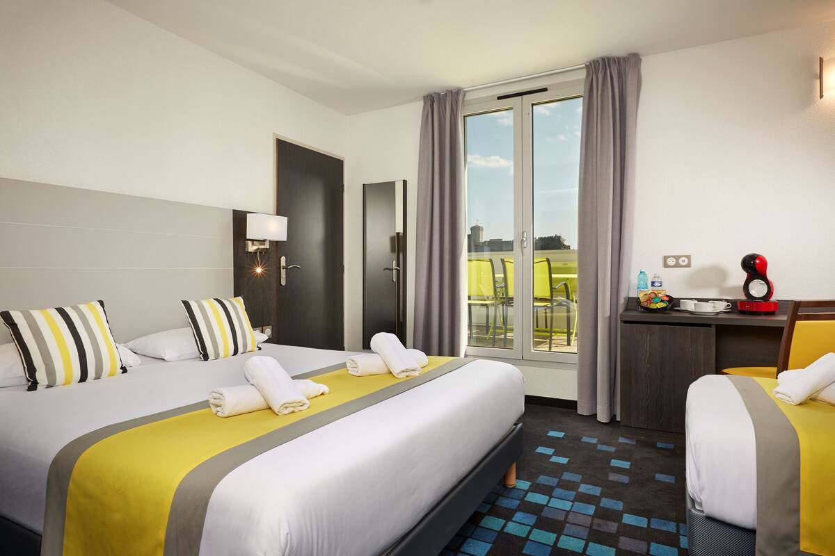 A hotel room with two beds, a desk, a chair, a window with curtains, and a view of the outside.