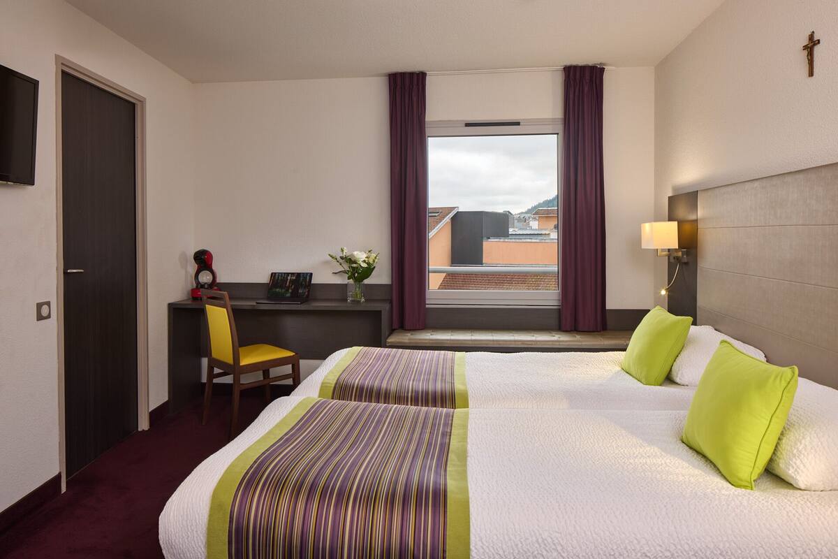 A hotel room with a bed, a desk, a chair, and a window with curtains.