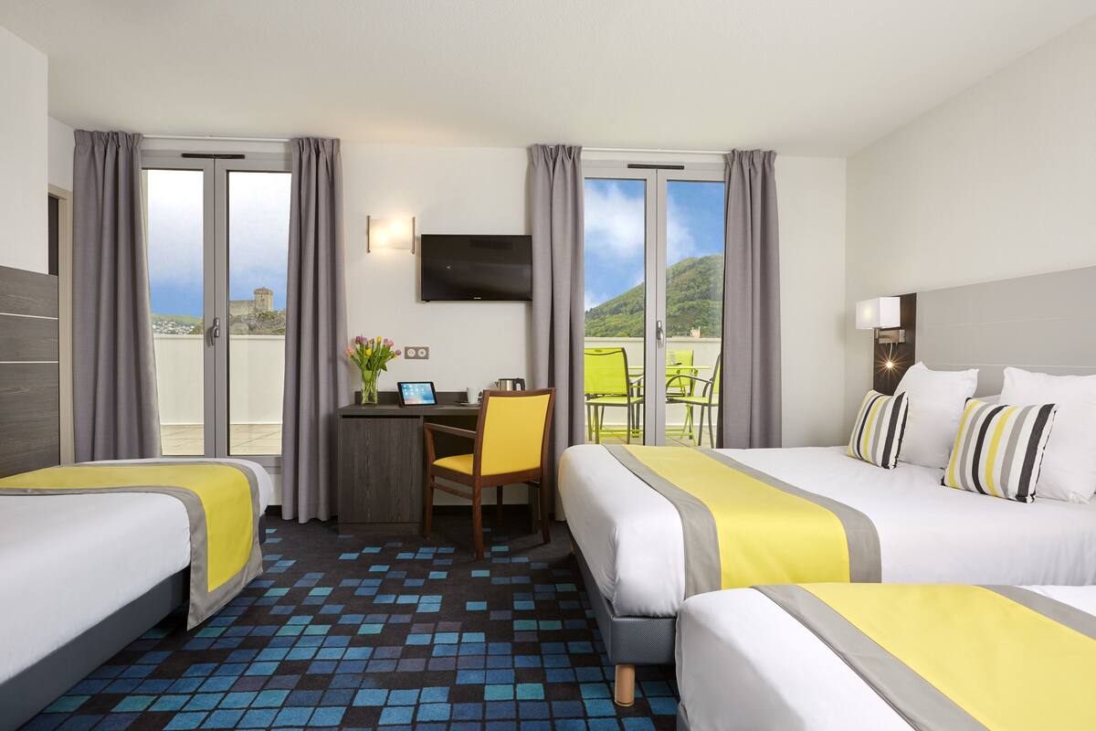 A hotel room with two beds, a desk, a chair, a TV, and a balcony with a view.