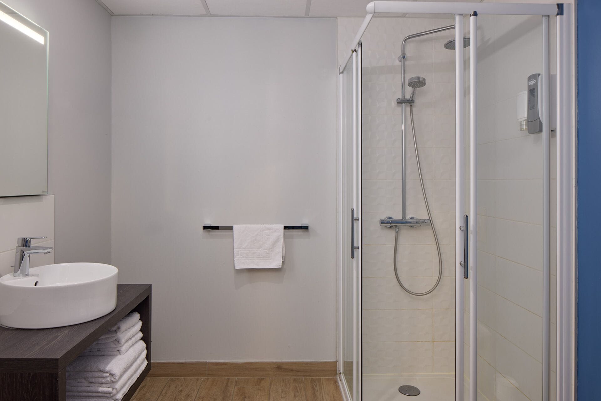 A modern bathroom with a glass-enclosed shower, a white sink, and a towel rack.