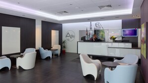 A modern hotel lobby with a reception desk, seating area, and a large screen. - Hôtel Astrid (Lourdes)