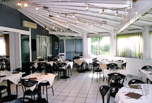 A restaurant with multiple tables and chairs, a tiled floor, and a ceiling with hanging lights. - Hôtel du Moulin à Vent (Venissieux)