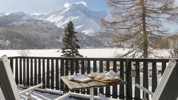 Eine Holzterrasse mit Teetisch, mit Blick auf eine verschneite Landschaft und Berge.