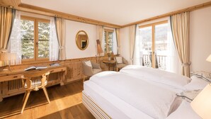 Ein Hotelzimmer mit einem großen Bett, einem Schreibtisch mit Stuhl, einem kleinen Tisch und einem Fenster mit Vorhängen.