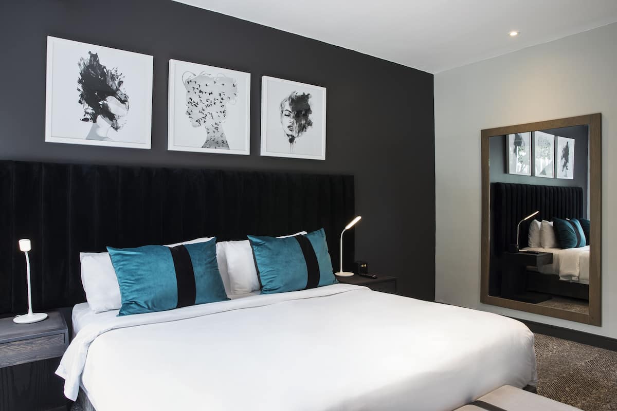 Een moderne hotelkamer met een groot bed, een donker hoofdbord en drie ingekaderde kunstwerken aan de muur.