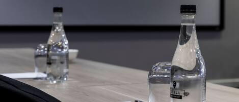 A conference table with two bottles of still water and a projector screen displaying "THE CAPITAL" with hotel, apartments, and resort services.