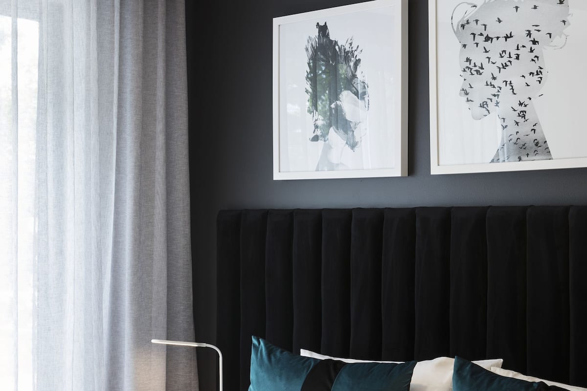 Een moderne hotelkamer met een groot bed, een donker hoofdeinde en twee kunstwerken aan de muur.