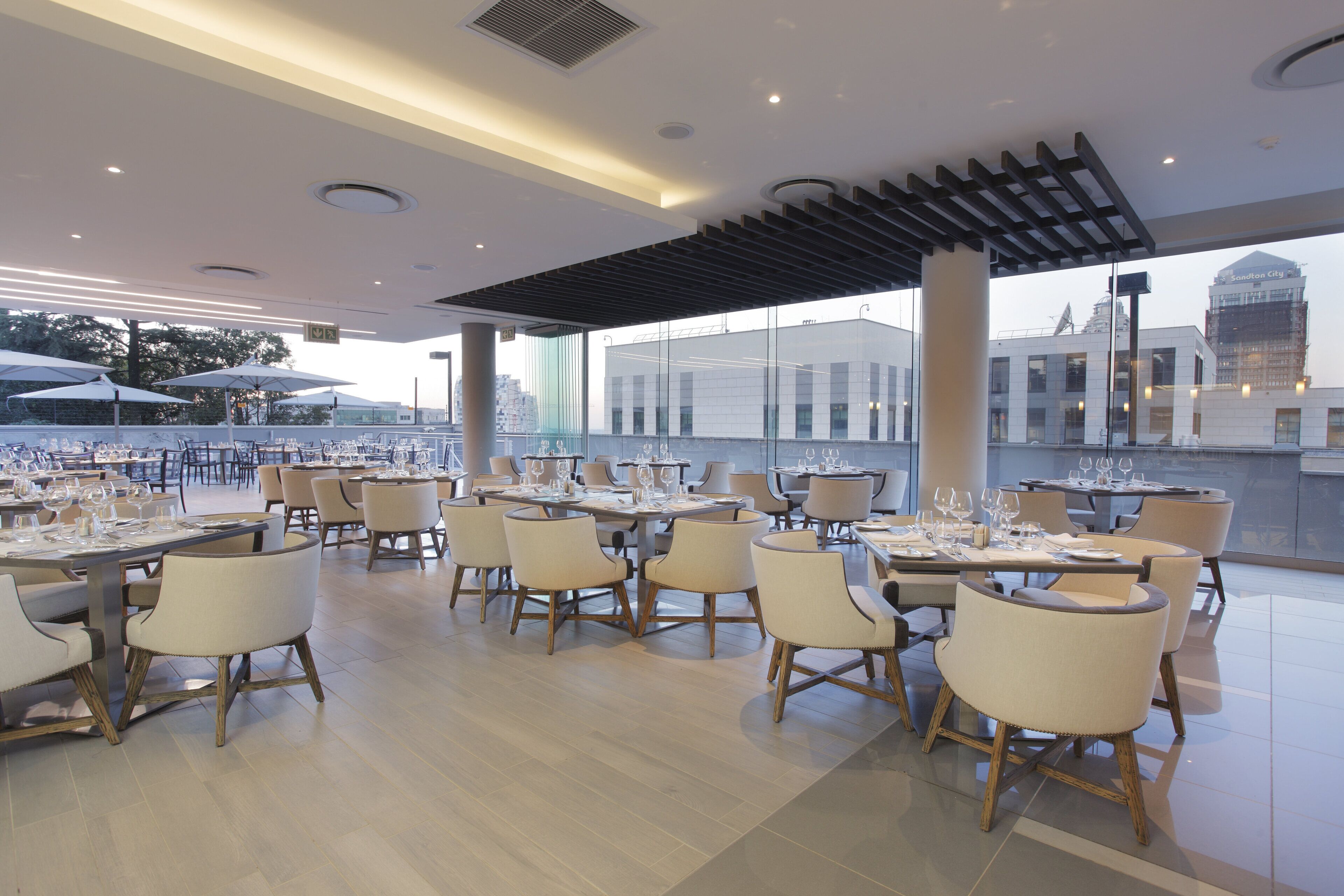 En moderne restaurant med flere spiseborde og stole, store vinduer samt udsigt over bybilledet.