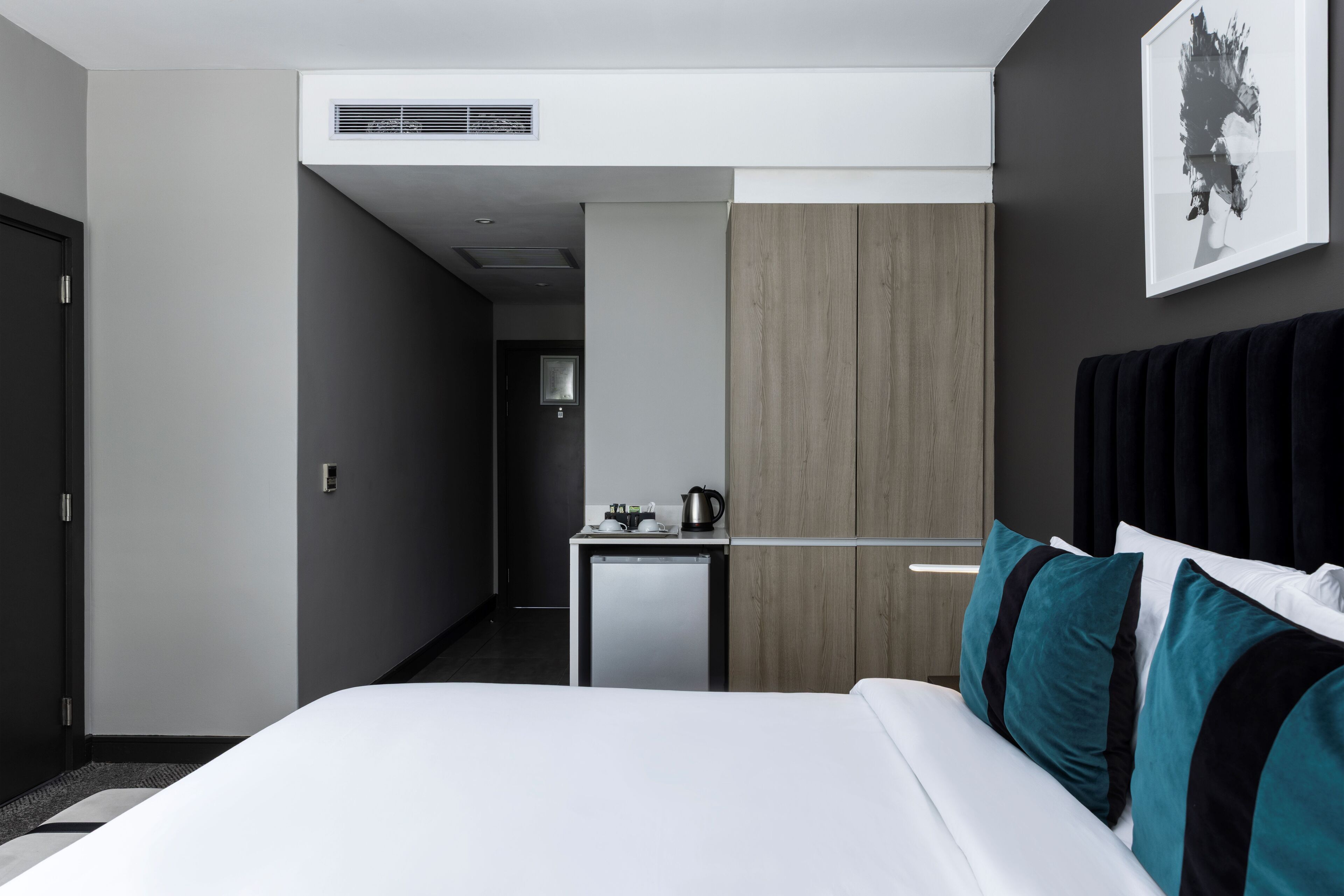 Habitación de hotel moderna con una cama, un escritorio pequeño, una tetera y una obra de arte enmarcada en la pared.