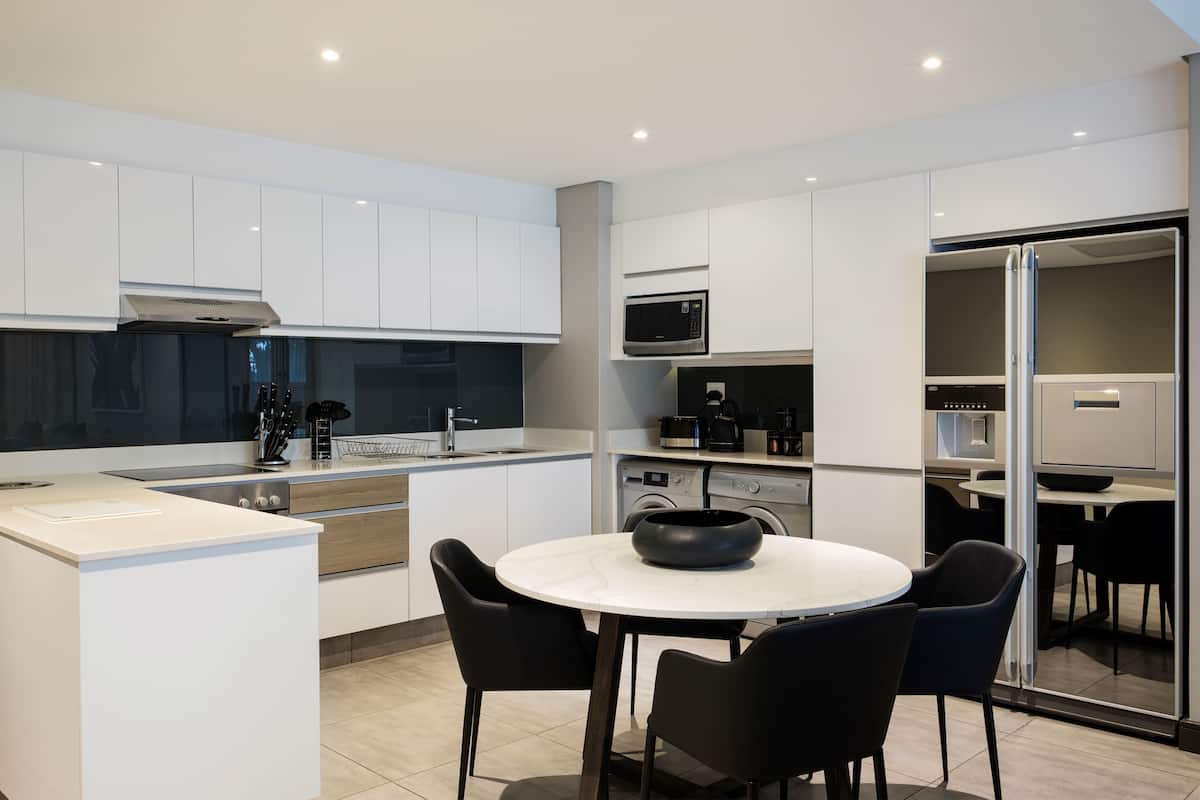 Een moderne keuken met witte kastjes, een magnetron, een fornuis en een eetgedeelte met een ronde tafel en stoelen.
