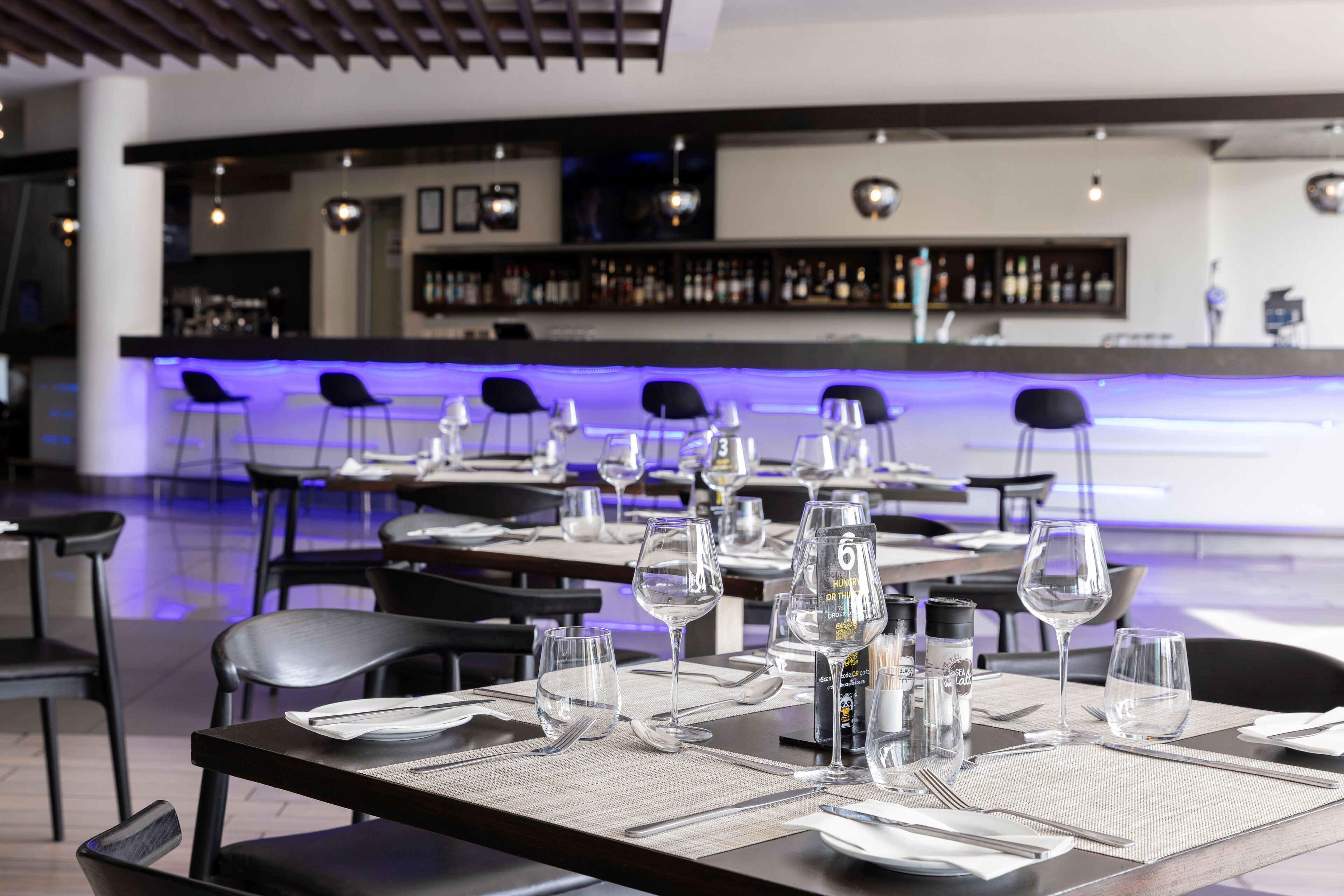 Ein Restaurant mit gedeckten Tischen, einer Bar im Hintergrund und einem modernen Interieur.