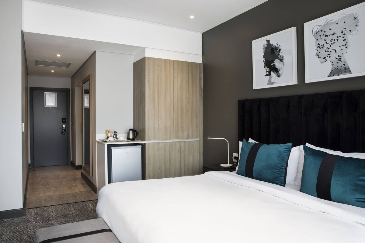 Een moderne hotelkamer met een groot bed, een bureau met waterkoker en twee ingelijste kunstwerken aan de muur.