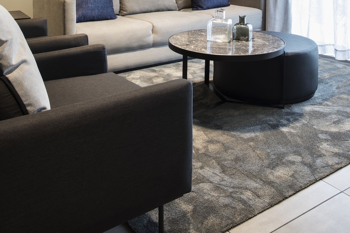 Een moderne woonkamer met een bank, fauteuils, een salontafel en een groot abstract schilderij aan de muur.