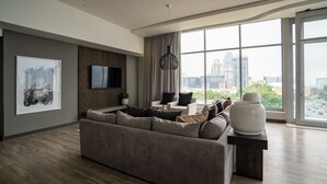 Un salon moderne avec un grand canapé, un téléviseur à écran plat et une grande fenêtre donnant sur la ville.