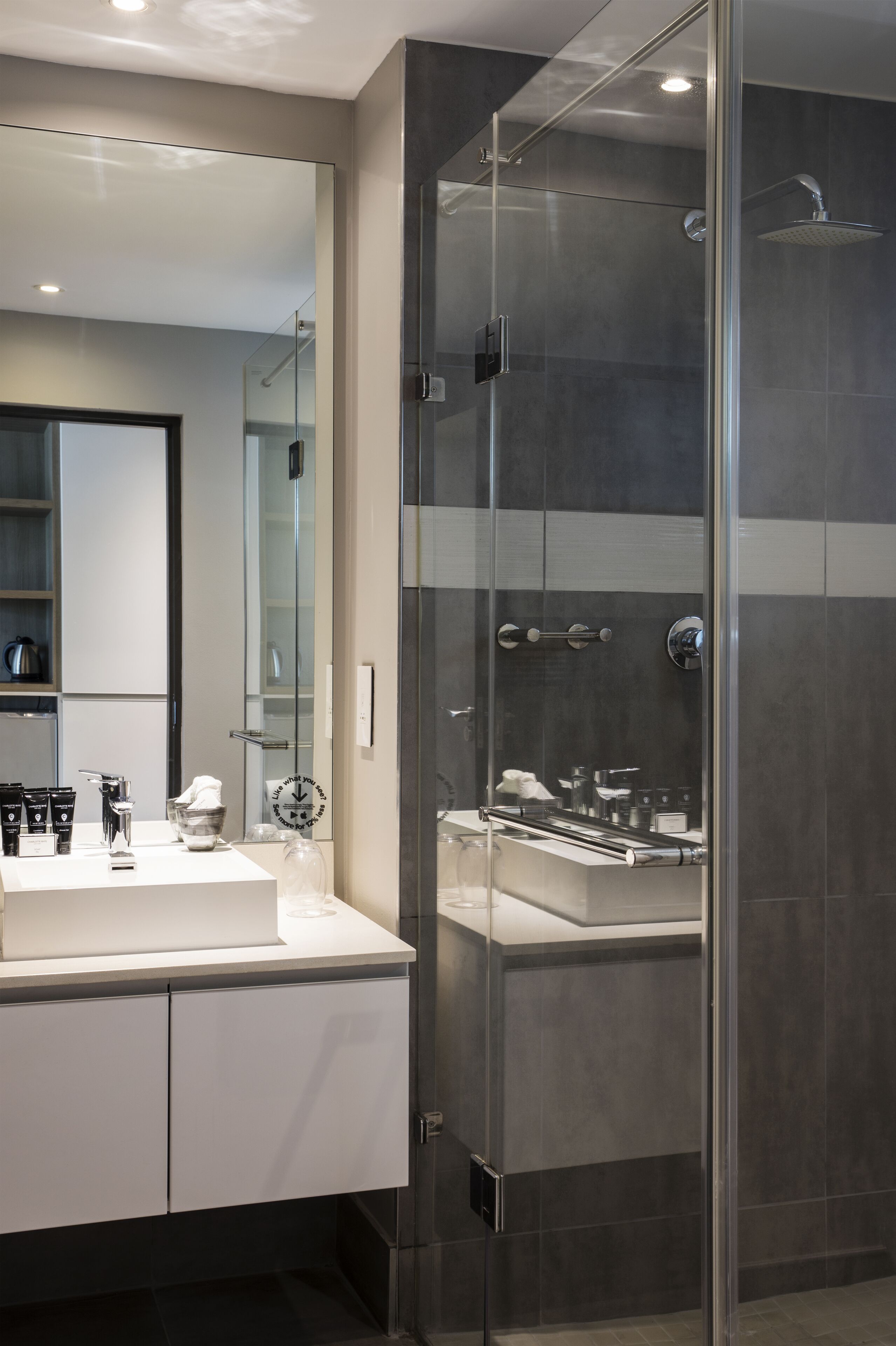 A modern bathroom with a glass-enclosed shower, a white vanity with a large mirror, and a dark tiled wall.