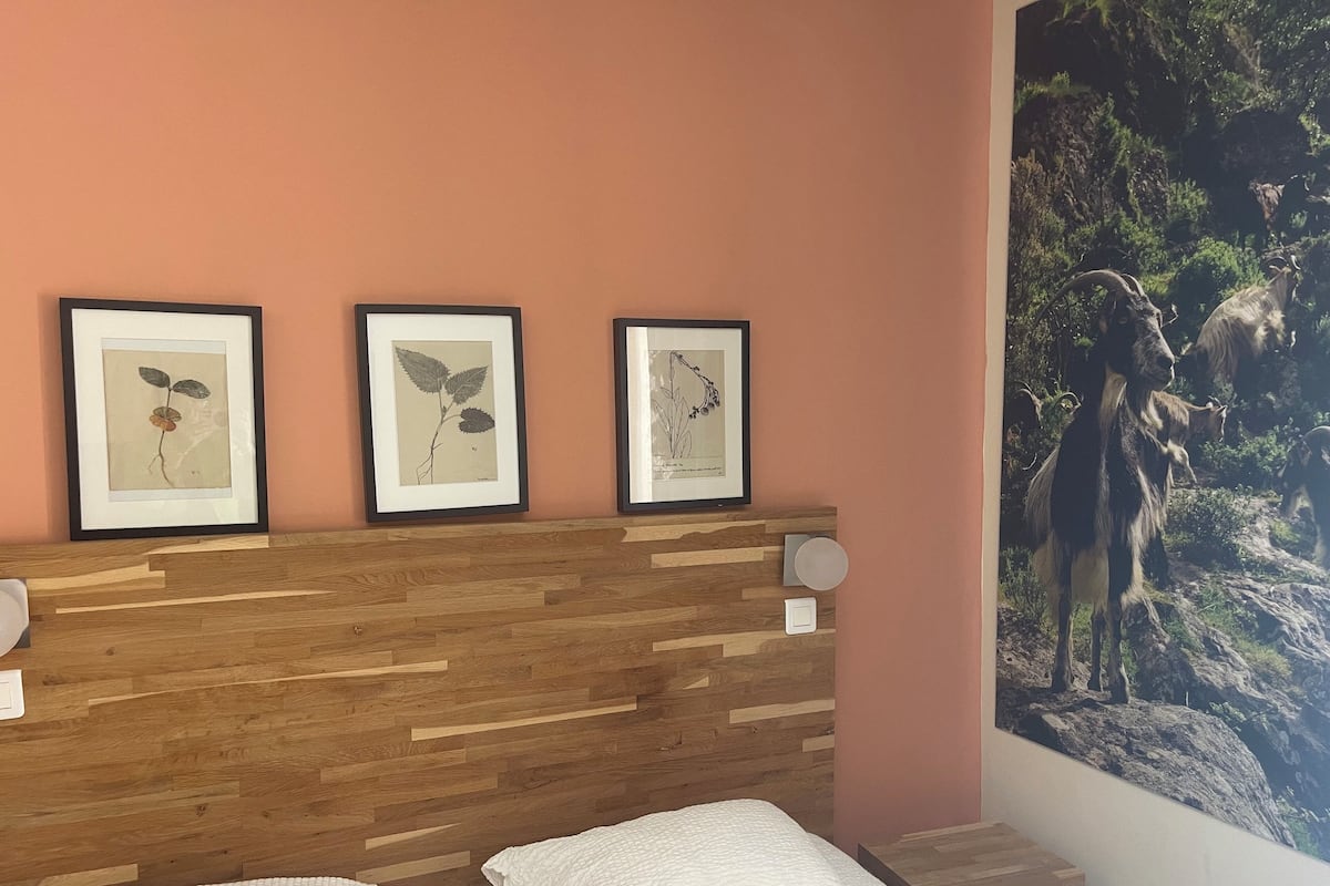 Une chambre à coucher avec une tête de lit en bois, un lit recouvert de linge de lit blanc et trois reproductions botaniques encadrées accrochées au mur.