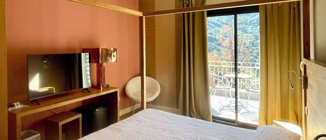 A hotel room with a bed, a TV, a desk, a chair, and a balcony with curtains.