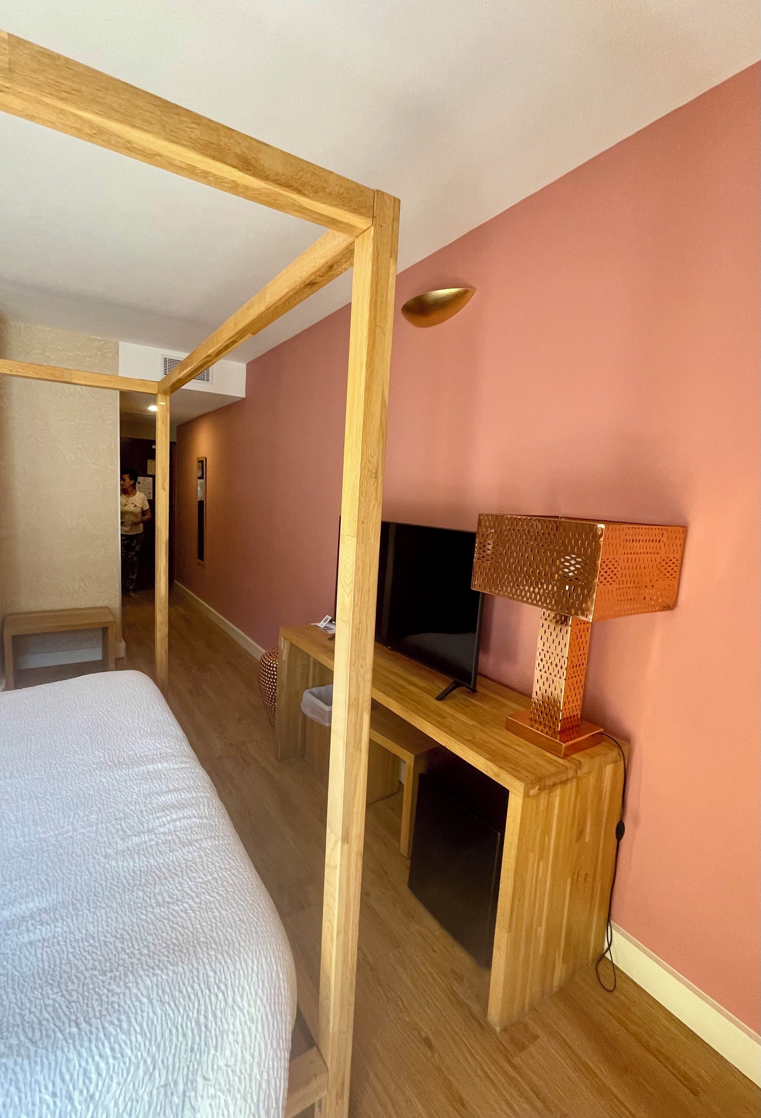 A bedroom with a bed, a desk, a TV, and a lamp.