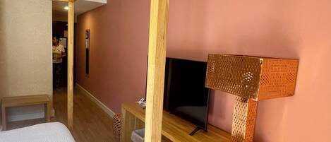 A bedroom with a bed, a desk, a TV, and a lamp.