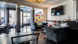 Een moderne hotel lobby met een kroonluchter, een flatscreen televisie, een zithoek met banken en een kleurrijk vloerkleed.