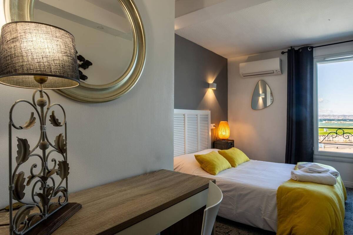 A hotel room with a bed, bedside lamp, and a view of the sea.