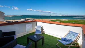 Een balkon met twee loungestoelen en een kleine tafel, met uitzicht op een strand en de zee.