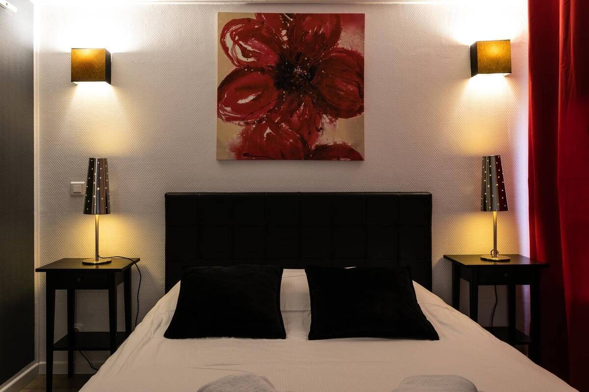 A hotel room with a large bed, two bedside tables, a wall-mounted painting, and two wall lamps.