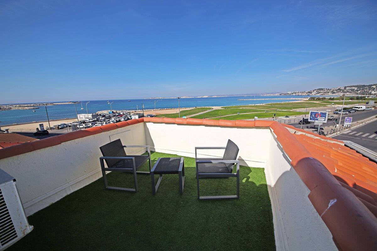 A rooftop terrace with two chairs and a table, overlooking a beach and cityscape.