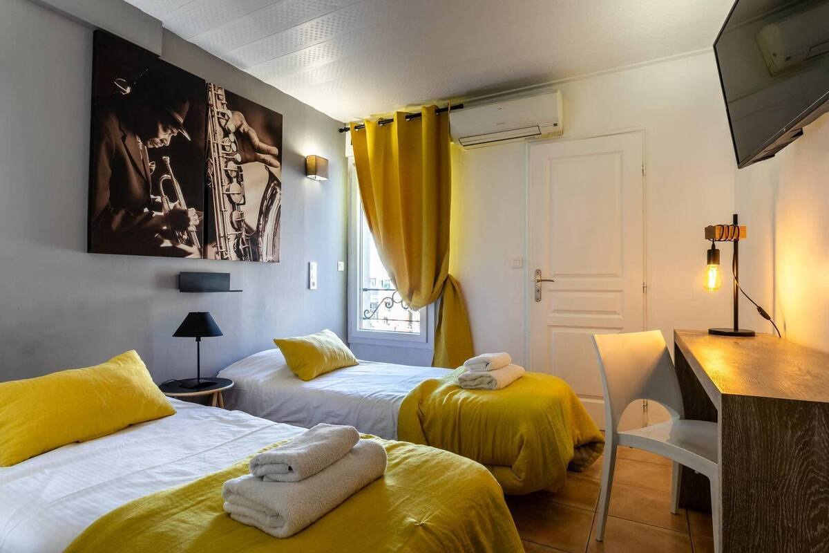 A hotel room with two beds, a desk, a chair, a TV, and artwork on the wall.