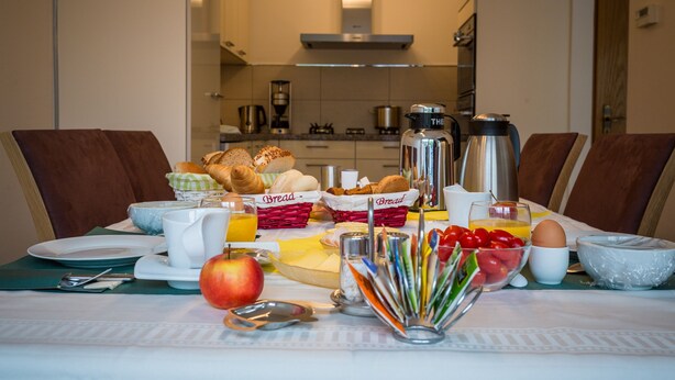 A breakfast table with bread, eggs, tomatoes, and a coffee pot.