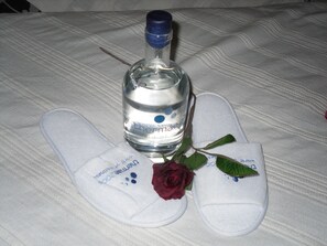 A bottle of water, a pair of slippers, and a rose on a bed.