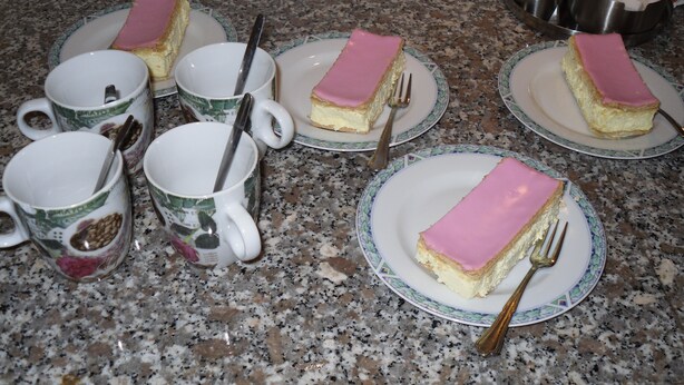 A kitchen counter with plates of pink-topped cheesecake and coffee mugs. - Rene's B&B (Kerkrade)