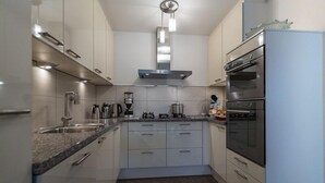 A modern kitchen with white cabinets, a granite countertop, a built-in oven, and a coffee maker.